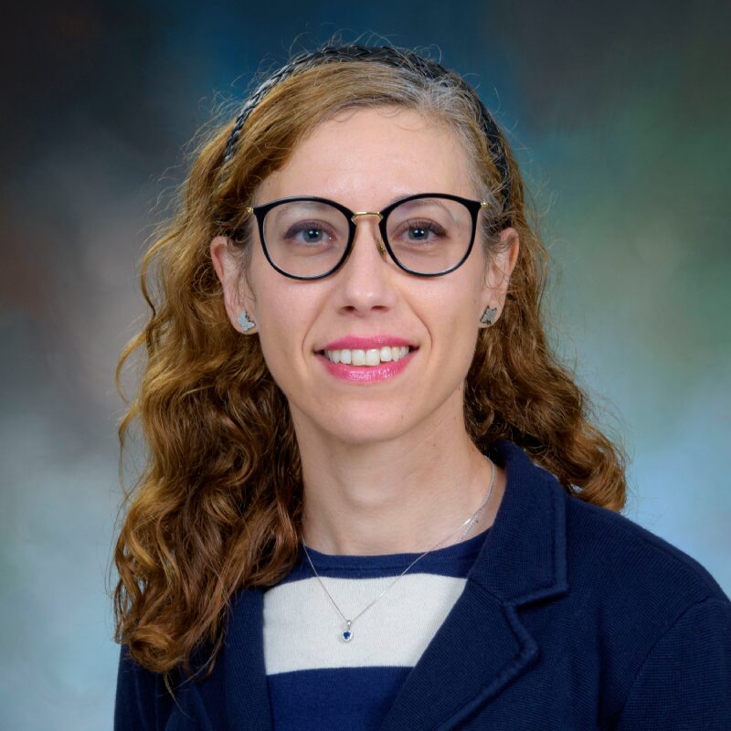Woman wearing glasses, smiling, with curly hair.