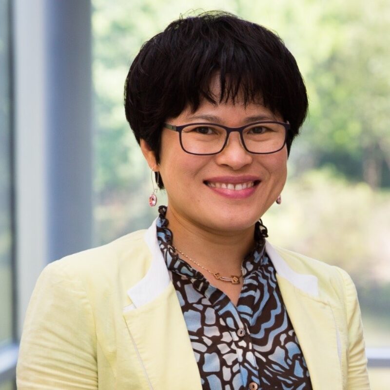 Smiling person wearing glasses and a blazer.