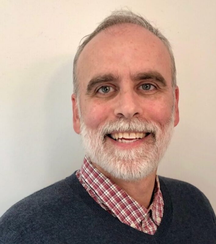 Smiling man with beard and checkered shirt.
